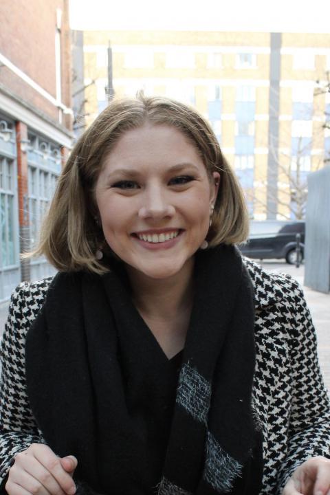 Headshot of Madison Wildey. She is looking directly into the camera and smiling. She wears a black and white jacket and a black scarf.